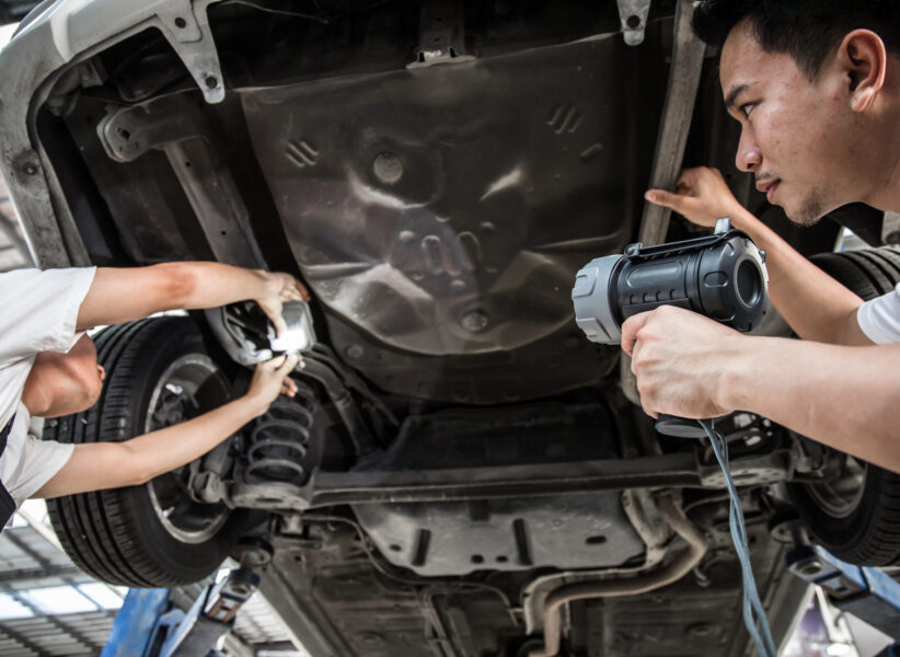 Two mechanic was checking the car suspension. Vehicle raised on lift at maintenance station. Car in service station with two men repair. Car mechanic working at automotive service center.