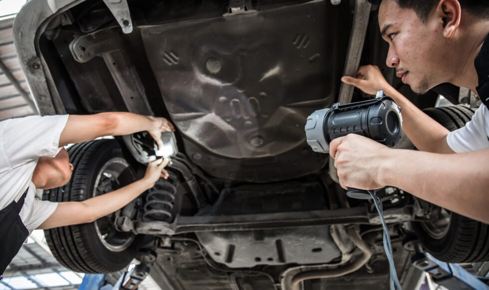 Two mechanic was checking the car suspension. Vehicle raised on lift at maintenance station. Car in service station with two men repair. Car mechanic working at automotive service center.